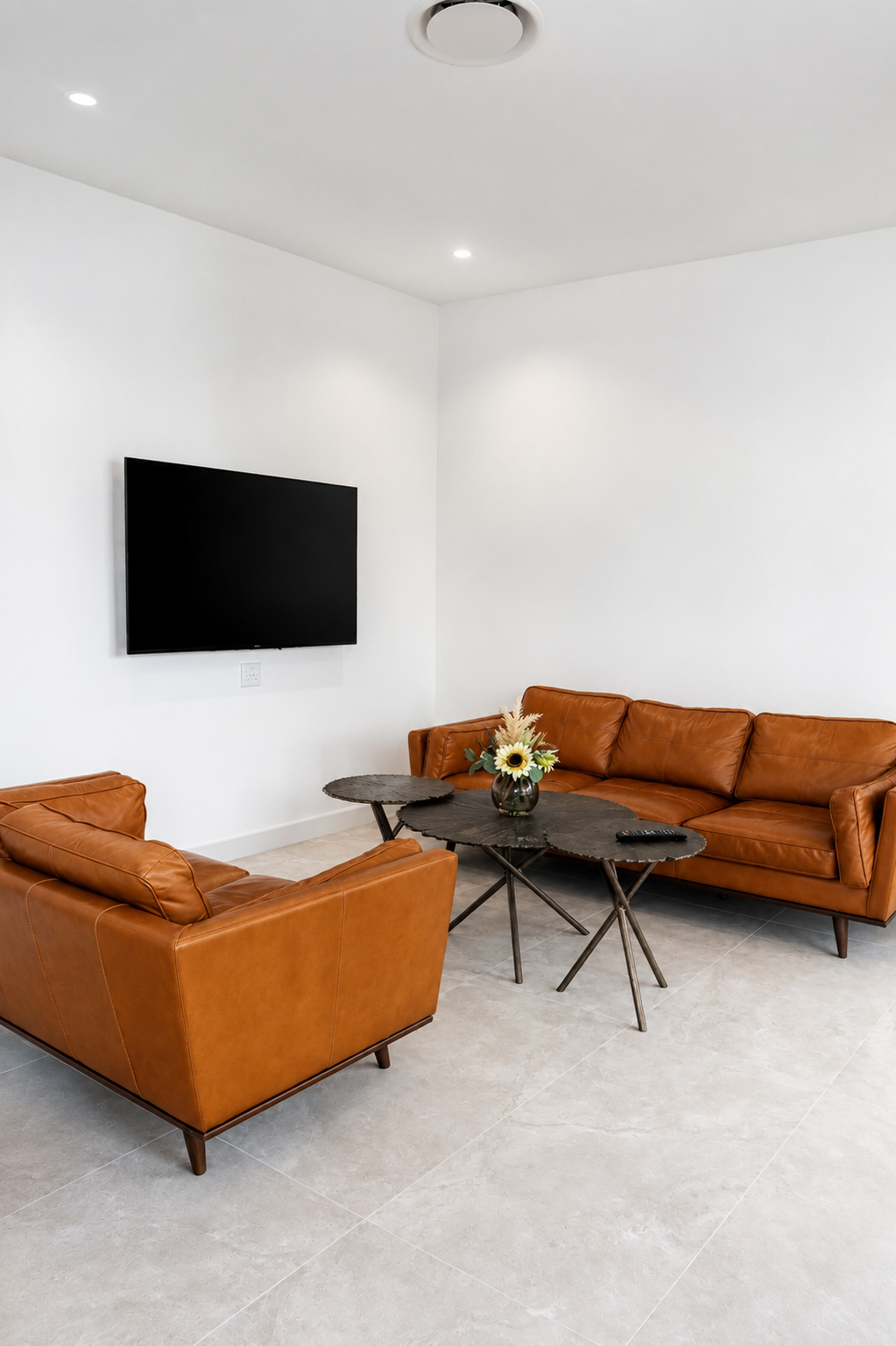 Bright living room with tan leather lounges and wall mounted TV